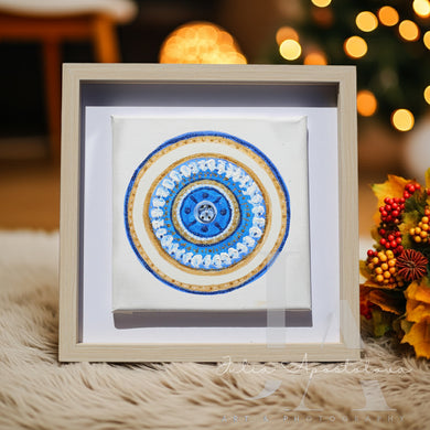 Framed mandala art piece with a blue and gold design on a soft surface with blurred festive background.