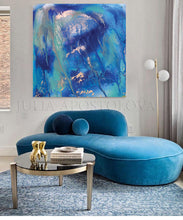 An abstract blue and teal canvas wall art print with gold accents hanging above a modern curved blue velvet sofa in a styled living room setting.