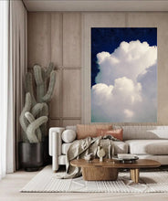 Large white cloud against a navy blue celestial sky painting , hanging over light colored couch , in modern minimalist boho living room setting. 