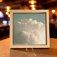 Framed photograph of a cloud on a wooden surface with blurred lights in the background
