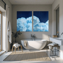 Modern bathroom with a freestanding bathtub, two large cloud paintings on the wall, and natural light.