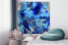A large abstract canvas wall art print featuring swirling shades of blue, teal, and metallic silver, displayed in a modern living room setting above a green beanbag chair and white rug.