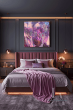A styled bedroom featuring a large square abstract painting with vibrant purple, pink, and blue brushstrokes, hung on a dark gray paneled wall above a bed with a mauve headboard and purple bedding. The artwork is signed 'JULIA APOSTOLOVA'.