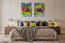 A modern bedroom scene with a bed dressed in beige bedding and colorful pillows, flanked by matching nightstands and pendant lights. Above the bed hang two vertical abstract paintings with vivid blue, green, yellow, and pink brushstrokes.