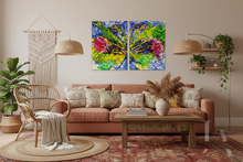 A two-panel abstract canvas wall art set featuring vibrant green, blue, and pink brushstrokes, displayed in a modern, bohemian-style living room above a terracotta sofa with patterned pillows.