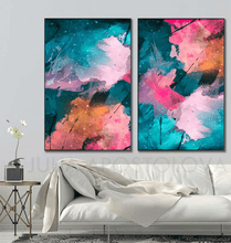 A pair of vertical framed abstract wall art prints hanging above a white sofa in a modern living room. The artwork features vibrant, painterly abstract designs in teal, pink, coral, and purple with white star-like speckles.