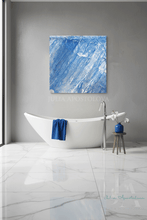 A modern bathroom scene with a white freestanding bathtub, a blue towel draped over the side, a chrome faucet, a small wooden stool with a blue vase of flowers, and a large abstract blue and white wall art piece above the tub.