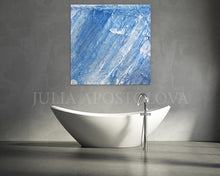 A square abstract canvas print with textured blue and white brushstrokes hangs on a gray concrete wall above a modern white freestanding bathtub with a chrome faucet. The watermark 'JULIA APOSTOLOVA' is visible across the center.
