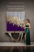 Woman in a green dress standing next to a modern console table with a large purple gray gold leaf abstract painting on a gray wall.