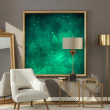 A large framed abstract art painting print featuring a vibrant emerald green and teal cosmic nebula with glowing stars, displayed on a dark gray wall in a modern living room setting with a white armchair, side tables, and a lamp.