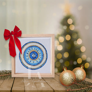 A framed original painting of greek eye with blue and white mandala design , placed on a wooden surface with Christmas ornaments and a blurred Christmas tree in the background. Ideal art gift for Christmas, Valentine's Day, Birthday, and any occasion. 