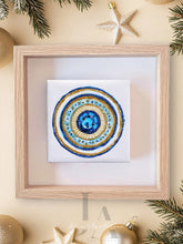 A colorful abstract mandala-like design with concentric circles in shades of blue , gold, and white against a neutral background. Perfect greek evil eye art gift for protection.