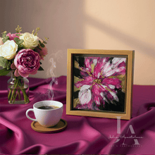 Framed abstract painting of a pink flower on a purple fabric with a cup of coffee and flowers.