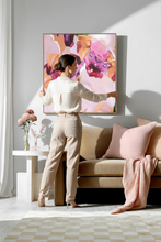 Woman standing in a living room with a large pink abstract painting on the wall.