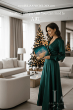 Woman in a green dress holding a framed painting, with a Christmas tree in the background