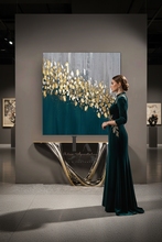 Woman in a dark teal dress standing next to a large gold leaf abstract painting in an art gallery. The painting ''Autumn Jewels'' with teal gold and gray colour scheme, is created by artist Julia Apostolova.