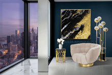 Modern interior with a cityscape view, beige armchair, and gold black abstract art on a dark blue wall.