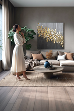 Woman in a white dress standing in a modern living room with a large abstract painting on the wall, with gold leaf, black and gray colors, painted by artist Julia Apostolova.