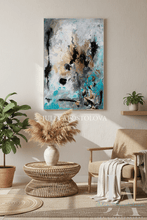 Abstract painting on a wall above a wicker table with decorative items in a living room, and plants.
