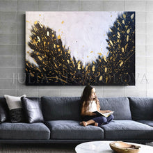 A chiled reading a book on a gray sofa with a large abstract gold leaf painting above it.
