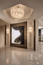 Modern interior with a large black white gold abstract painting on a wall, decorative elements, ceiling light fixture, chandelier, and wall sconces.