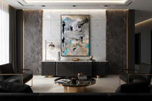 A large vertical abstract canvas with gold leaf, black, gray, and turquoise / teal brushstrokes, displayed in a modern living room setting above a dark gray sideboard.