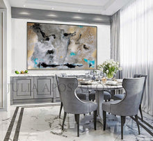 A large abstract canvas painting with gray, black, and gold tones hangs on a white wall above a gray dining cabinet and dining table set with gray chairs in a modern dining room.