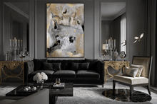 A large vertical abstract canvas print with gold, white, and black textures hangs on a dark gray paneled wall above a black sofa in a luxury modern living room.