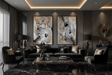 A luxury modern living room featuring a black leather sofa and two matching armchairs, decorated with black and gold abstract wall art panels. The room has a dark gray wall, a black marble coffee table, and warm recessed lighting in the ceiling.