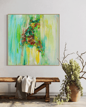 Abstract canvas wall art featuring a green, yellow, and brown brushstroke design, displayed in a styled room setting above a rustic wooden bench with a draped throw blanket and next to a large ceramic vase with dried branches.
