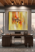 A large square abstract painting with vibrant yellow, orange, and red brushstrokes hangs on a gray wall above a dark wood office desk in a modern office setting.