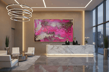 A large abstract painting with vibrant pink, magenta, and purple tones hangs on a beige wall in a modern lobby. The lobby features a marble reception desk with two staff members behind it, white lounge chairs, a large ring chandelier, and floor-to-ceiling windows.