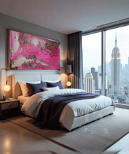 A modern bedroom featuring a large, vibrant pink and gold abstract canvas painting above a white bed with purple accents, set against a gray wall with a large window overlooking a city skyline.