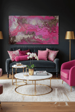 A large rectangular abstract wall art piece with vivid pink, magenta, and metallic gold marbling, displayed above a dark gray sofa in a styled living room with pink and gold furniture accents.