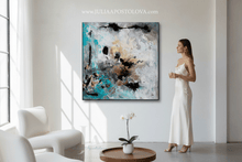 Woman in a white dress standing in a modern living room with an abstract painting on the wall. The gold leaf abstract painting is painted by artist Julia Apostolova