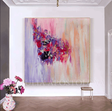 A large abstract canvas painting with expressive brushstrokes in pink, purple, red, blue, and peach tones, displayed on a white wall in a styled room with a small stool and a vase of flowers.