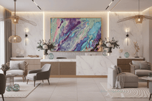 A large abstract canvas art print with swirling purple, blue, teal, and pink paint patterns, framed in gold, hanging on a white marble wall in a modern, stylishly decorated living room.