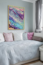 Abstract fluid art canvas print with swirling purple, blue, pink, and green paint patterns, displayed on a light gray wall above a bed with pastel pillows.