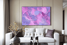 A large framed abstract wall art print featuring swirling pink, purple, and lavender marbled patterns, displayed above a white sofa in a modern living room setting.