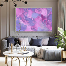 A large framed abstract canvas print with swirling pink, purple, and blue paint patterns hangs on a gray wall above a modern gray sectional sofa in a styled living room.