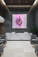 A large square abstract painting with pink, purple, and white brushstrokes and a floral motif in the center, displayed on a dark gray wall above a white marble reception desk in a modern lobby.