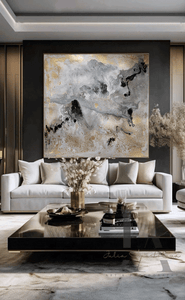 Modern Living room with large canvas in gray gold black and real gold leaf beautiful details, that shimmer under the different lighting, hanging over light colored couch , on dark gray wall, creating a glam atmosphere. The room features low modern coffee table and decorative elements, like vases candles and book. 