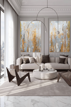 Modern living room with two large neutral abstract paintings, gray sofa, and stylish chairs.