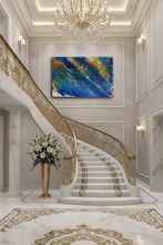 An abstract canvas painting with vibrant blue, gold, and white brushstrokes, displayed on a light gray wall in a luxurious grand staircase foyer with marble floors and a gold chandelier.