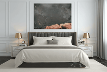 A modern bedroom featuring a large abstract wall art print with black, gray, and dusty pink tones, hung above a neatly made bed with white linens and a dark gray upholstered headboard.
