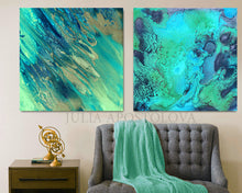 Two abstract paintings by Julia Apostolova hanging on a wall above a gray sofa with a green blanket.