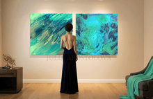 Woman in a dark dress standing in front of two large abstract teal blue paintings on a wall.