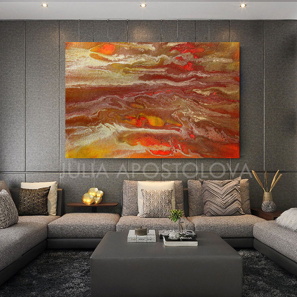 A modern living room featuring a large beige gay curved sofa with textured fabric, accompanied by a large gray pouf coffee table.  The wall behind has a large abstract painting depicting abstract desert ripples with warm neutral copper gold and orange tones . The room has large windows allowing natural light , and the decor includes plants and a dark gray-colored rug on the floor. The overall aesthetic is cozy and contemporary.