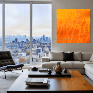 A large abstract orange painting on the wall , displayed in a modern living room with a large window overlooking a cityscape .  The room has a neutral color scheme with a large light gray sofa, gray and black pillows, a low wooden coffee table, and a gray rug on the floor.