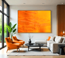 A large orange minimalist painting , displayed on white wall in a modern living room with a white sofa, two orange armchairs , a black low coffee table and a large window overlooking a natural landscape , creating a warm and inviting atmosphere